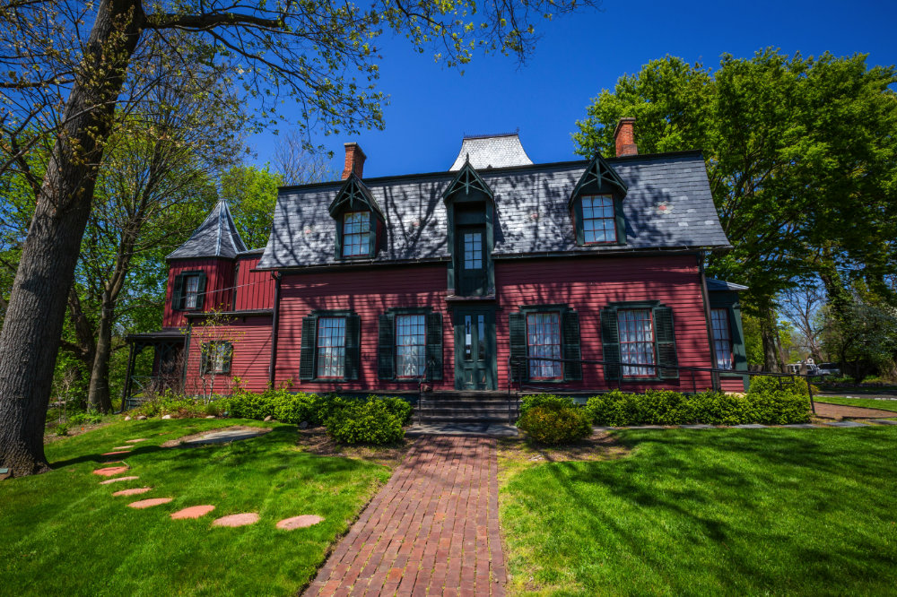 historical red gothic home with a walkway, lawn and trees
