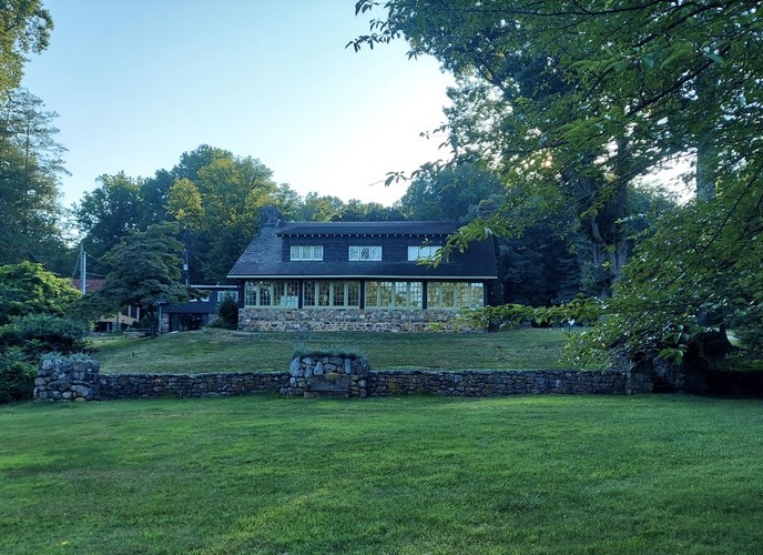 a rustic, T-shaped log house built with natural materials like chestnut timbers and fieldstone, topped by a large, gabled roof with long shed dormers and a ceramic tile roof.